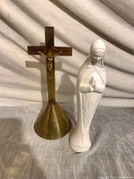 Brass crucifix and white Mary statue side by side