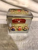 Front view of silver tin with angel motif and red music window