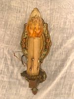 Front view of ornate gold wall sconce with faux candle and amber bulb
