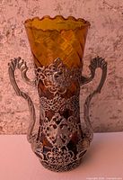 Front view showing amber glass body, twin pewter handles, filigree overlay with eagle motif