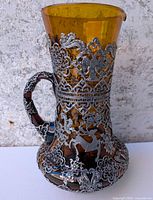 Front view showing amber glass body with pewter filigree overlay and handle