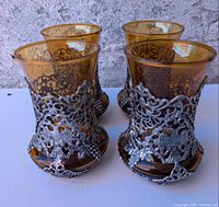 Front view of four amber tumblers showing pewter overlays and eagle motifs