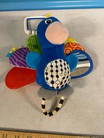 Front view of plush bird toy showing teether, mirror, textured wings, and clip