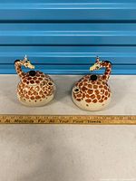 Both giraffe teapots side by side with ruler for scale