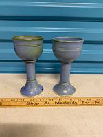 Two blue-green glazed pottery goblets standing side by side with ruler for scale