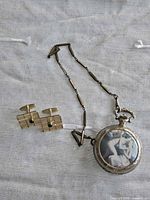Front view of pocket watch pendant with chain and pair of cufflinks