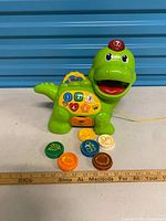 Full view of dinosaur toy with discs and ruler for scale