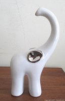 Front left view showing white ceramic elephant with silver ear and upward trunk