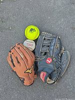Both gloves, softball and baseball grouped on pavement