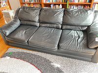Front view of black faux leather sofa showing three seats and back cushions
