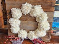 Front view of rustic wood panel with white pom-pom wreath decoration