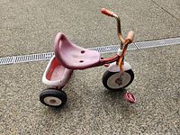 Left side view of red and white Radio Flyer tricycle showing seat, rear bin, wheels