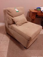 Front angled view of beige armless chaise lounge with pillow