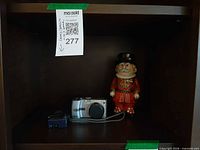 Camera, charger and Beefeater coin bank on shelf