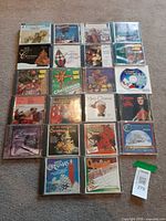 Full group of approximately twenty holiday music CDs arranged on carpet