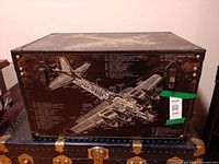 Front view of trunk showing blueprint graphic, metal latches, riveted corners