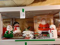 Shelf with Santa cookie tray box, plush Santa, snowman jar, metal sleigh, snowflake topper, ornaments