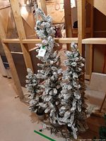 Three slim snow-flocked artificial trees standing together