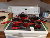 Full set of red KitchenAid pots and pans with lids on stovetop