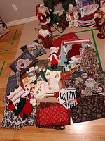 Overview of entire lot on floor showing Santa figurines, pillows, numerous stockings, aprons, placemats and other linens