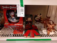 Shelf view showing all items: boxed snow globe, bobble Santa box, Santa and reindeer figurines, spreaders box, glass star dish