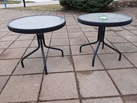 Both round black glass-top tables side by side showing frames and legs