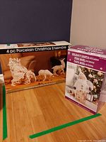 Both boxed sets: Grandeur Noel 4-pc Porcelain Christmas Ensemble and Kirkland Signature Holiday Santa with Lantern