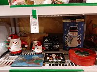 Shelf view showing Santa cookie jar, smaller Santa pieces, glass trivet, coaster stack, boxed snowman jar and red tin
