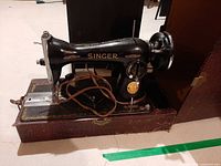 Left side view of Singer sewing machine in base showing decals, cord, and mechanical components