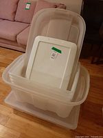 Stacked clear plastic bins with white lid in front of sofa