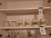 Six mugs on upper cupboard shelf, four with printed scenes, two plain with blue stripes