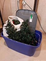 Blue tote containing two artificial Christmas trees, bag of decorations, grey lid