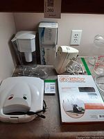 Overall lot showing mixer, water pitcher and box, sandwich maker, EZ Glider box, glass pitcher and measuring cup