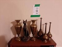 Front view of all five brass vases and Bastet figurine on shelf