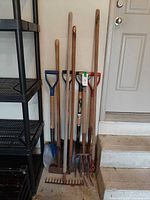 Overall group of long-handled garden tools leaning against wall
