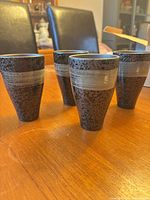 Four speckled black ceramic mugs with silver band on wooden table