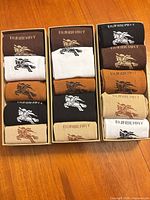 Open view of three boxes showing fifteen folded pairs of Burberry logo socks in various colours