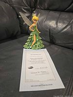 Tinkerbell figurine next to COA on black leather surface