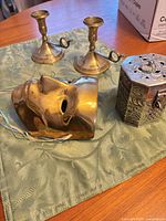 Full lot showing candlesticks, brass mask and silver-plate canister on cloth