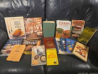 All sixteen cookbooks arranged on a sofa showing titles and varied bindings