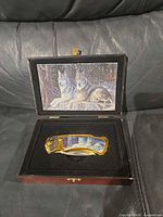 Knife in open wooden box showing wolf artwork on handle and inside lid