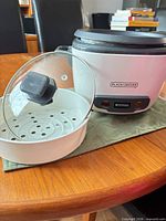 Front view of Black+Decker rice cooker with glass lid and steaming basket displayed