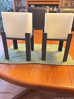 rear view of two black metal stands with white wax cube shades