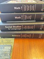 Stack of four black curriculum binders labeled Math, Math, Social Studies & Language, Science
