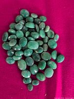 Pile of approximately 50 loose green faceted oval gemstones on magenta background