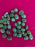 Group of oval green gemstones scattered on magenta surface