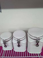 Front view of three graduated white ceramic canisters with clamp lids