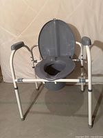 Front view of commode showing seat, lid up, bucket, armrests, adjustable legs