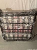 Folding metal bed frame with mattress wrapped in plastic, front view