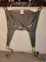 Full view of grey sling with green straps laid out flat
